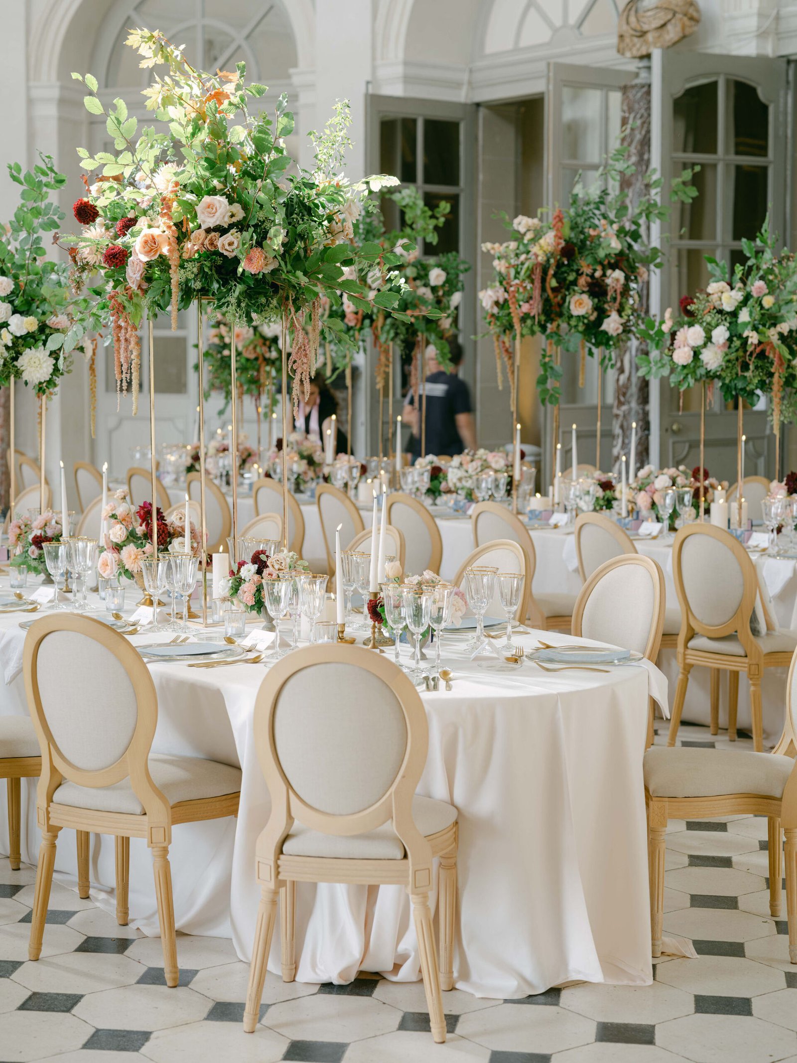 Reception dinner at Château de Vaux-le-Vicomte with tall floral centerpieces and candlelight in a gilded salon during golden hour