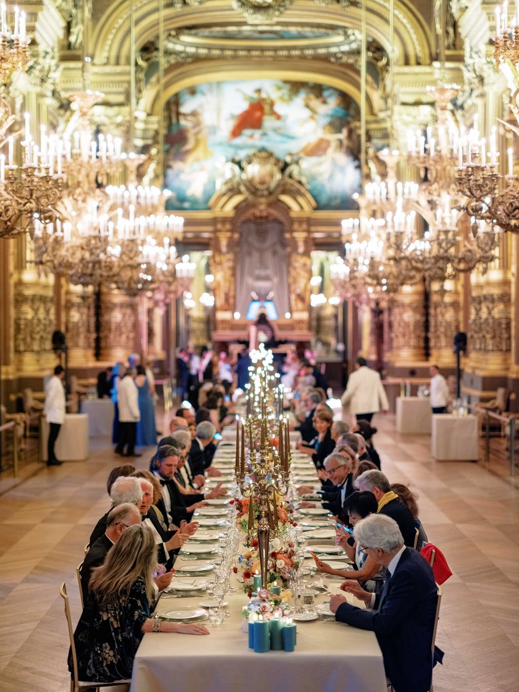 Wedding reception dinner in Palais Garnier grand foyer with crystal chandeliers and ornate gilded ceiling