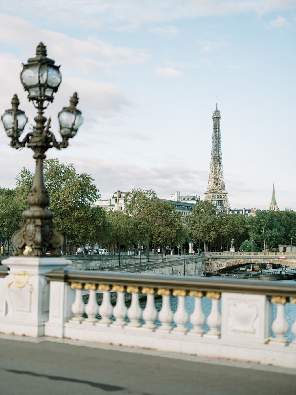 Eiffel Tower seen from Pont Alexandre III bridge with ornate lamppost and stone balustrade in morning light