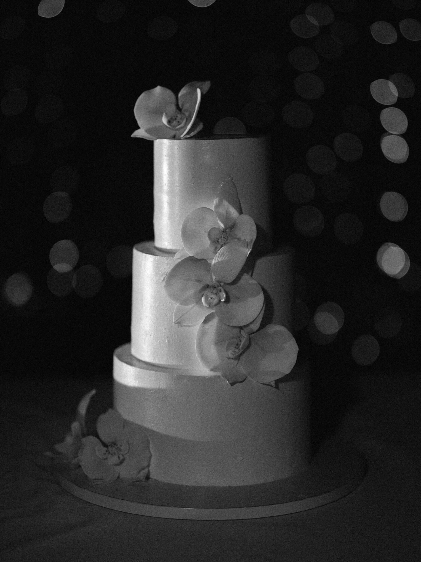 Three-tier wedding cake with orchid cascade and dramatic bokeh at Château de la Durantie