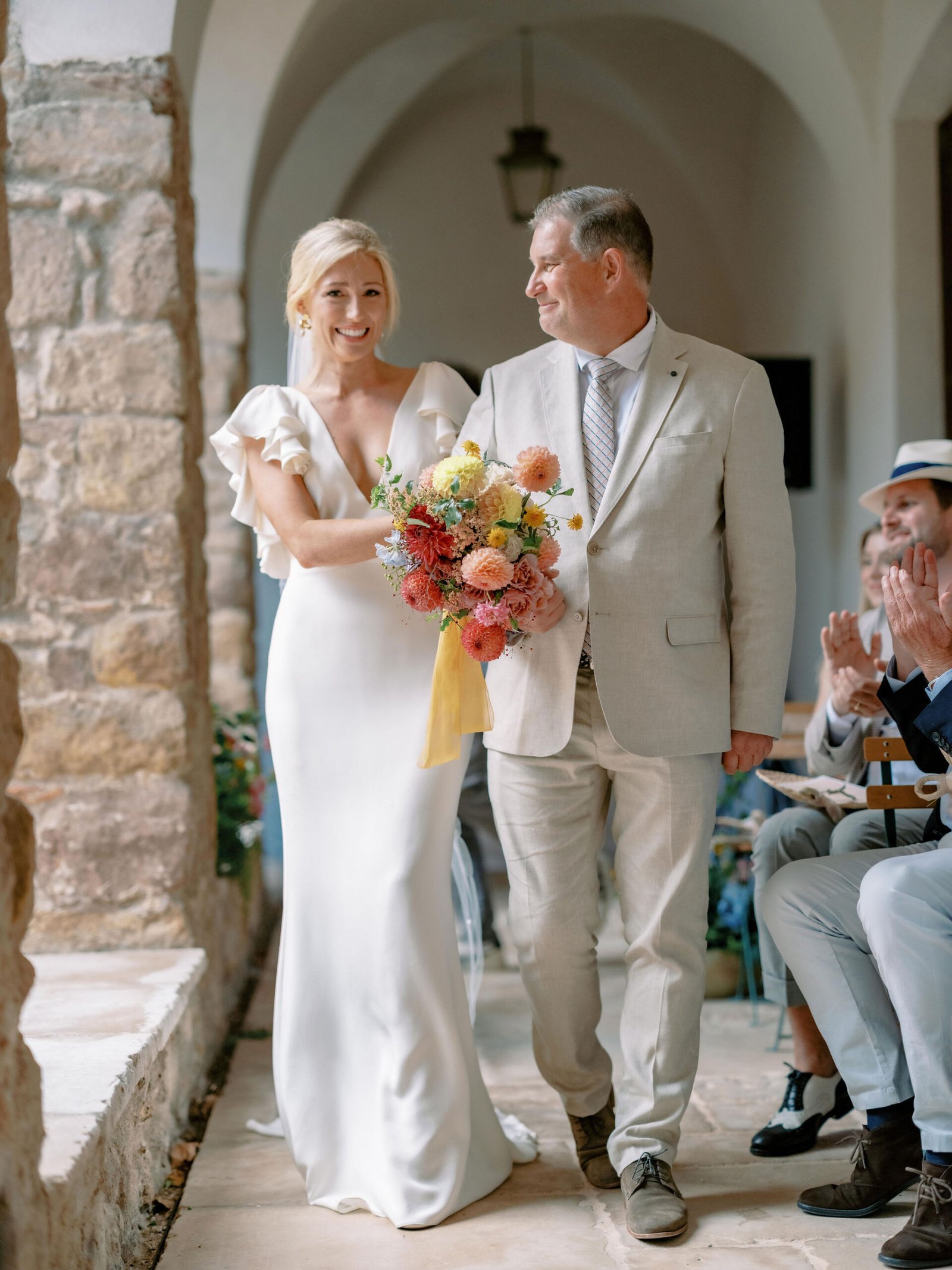 Bride walking down the aisle with her father under stone arches at Chateau Sainte Roseline ceremony in Provence