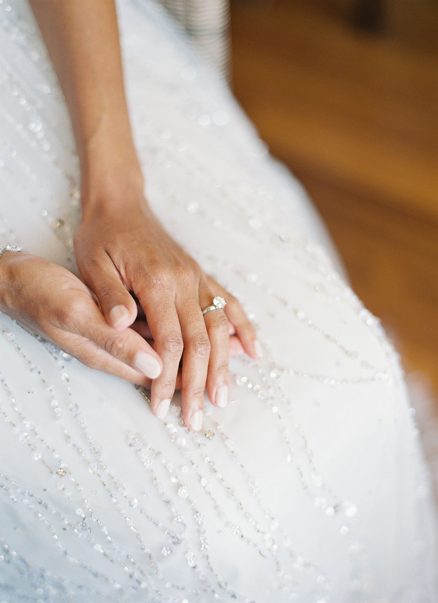 Bride's hands with engagement ring resting on beaded wedding gown at Pan Deï Palais Saint-Tropez in golden light
