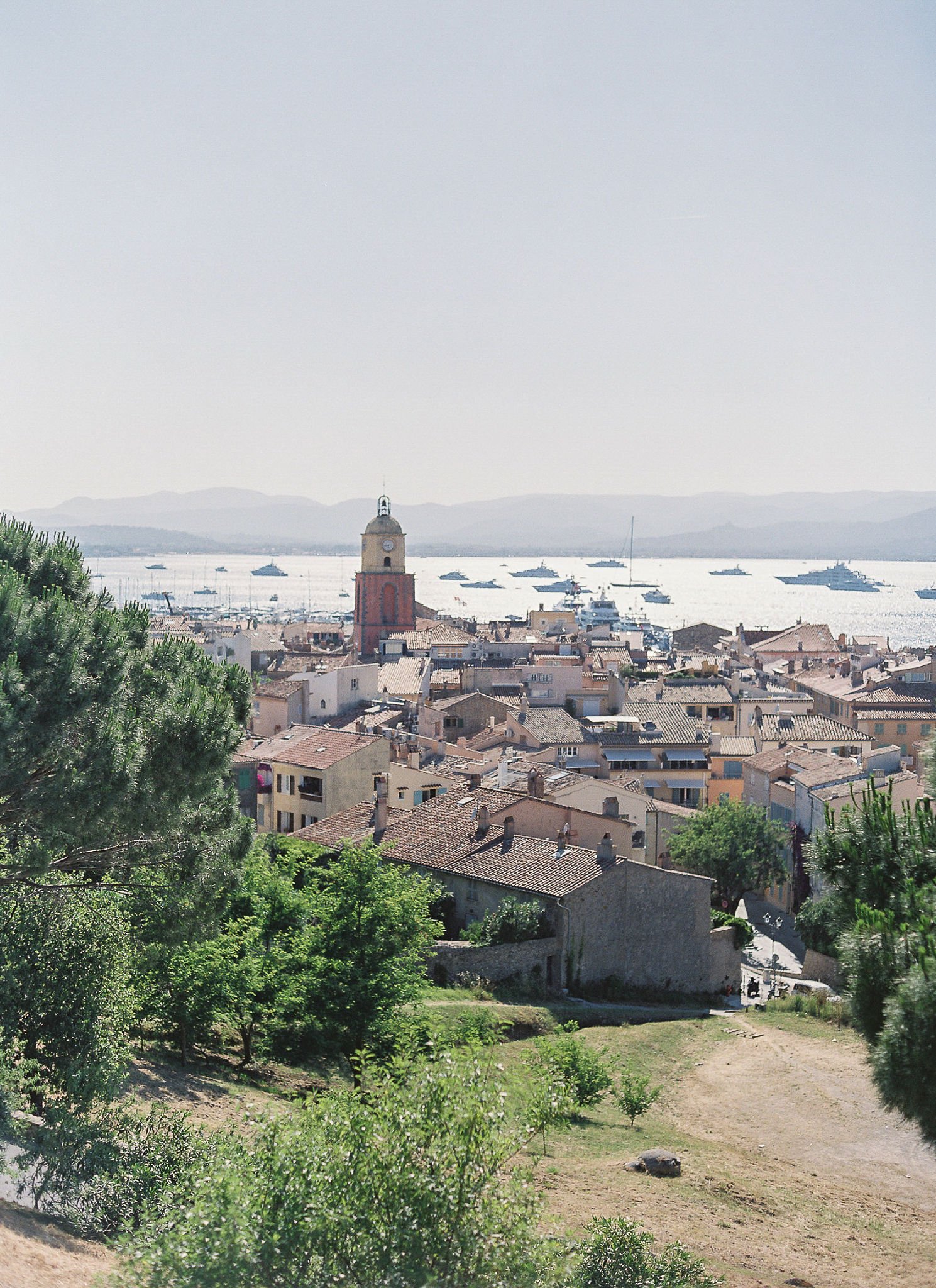 Panoramic view of Saint-Tropez village with historic bell tower overlooking Mediterranean yachts at golden hour