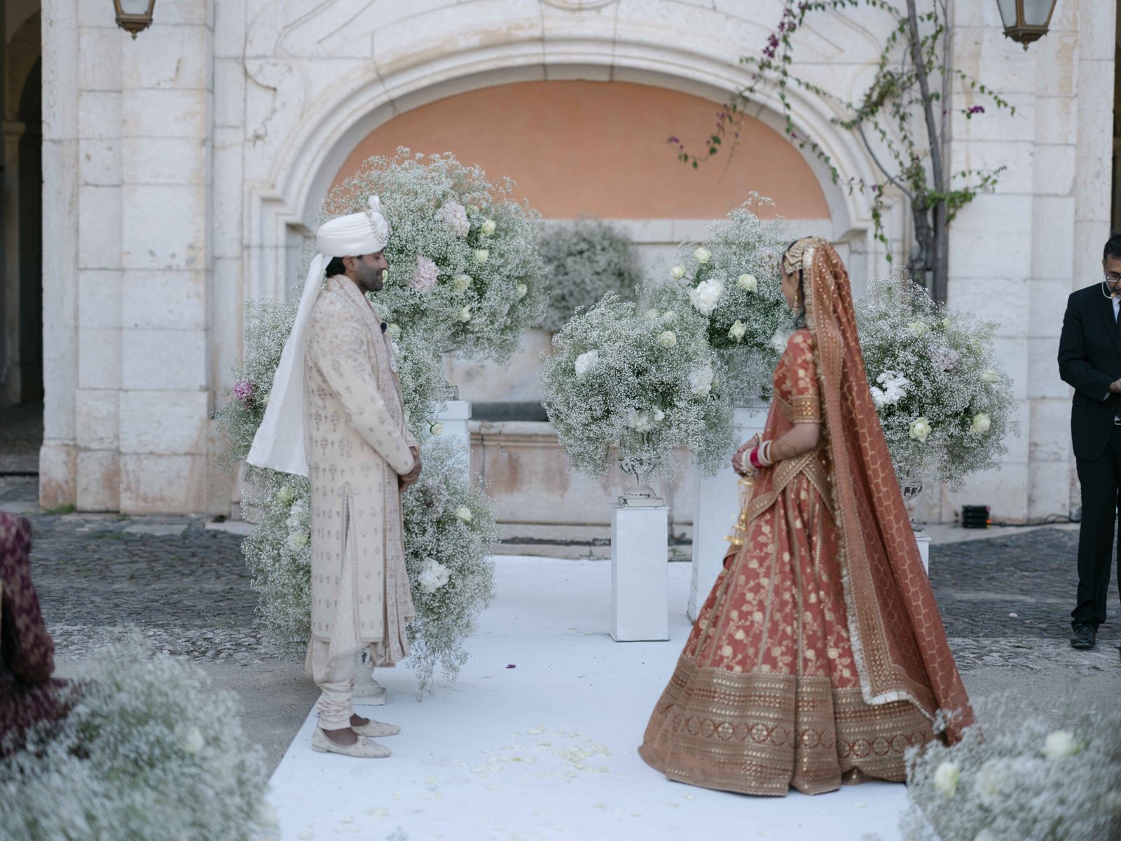 Indian bride and groom under a baby's breath arch at their wedding ceremony in Lisbon, soft evening light