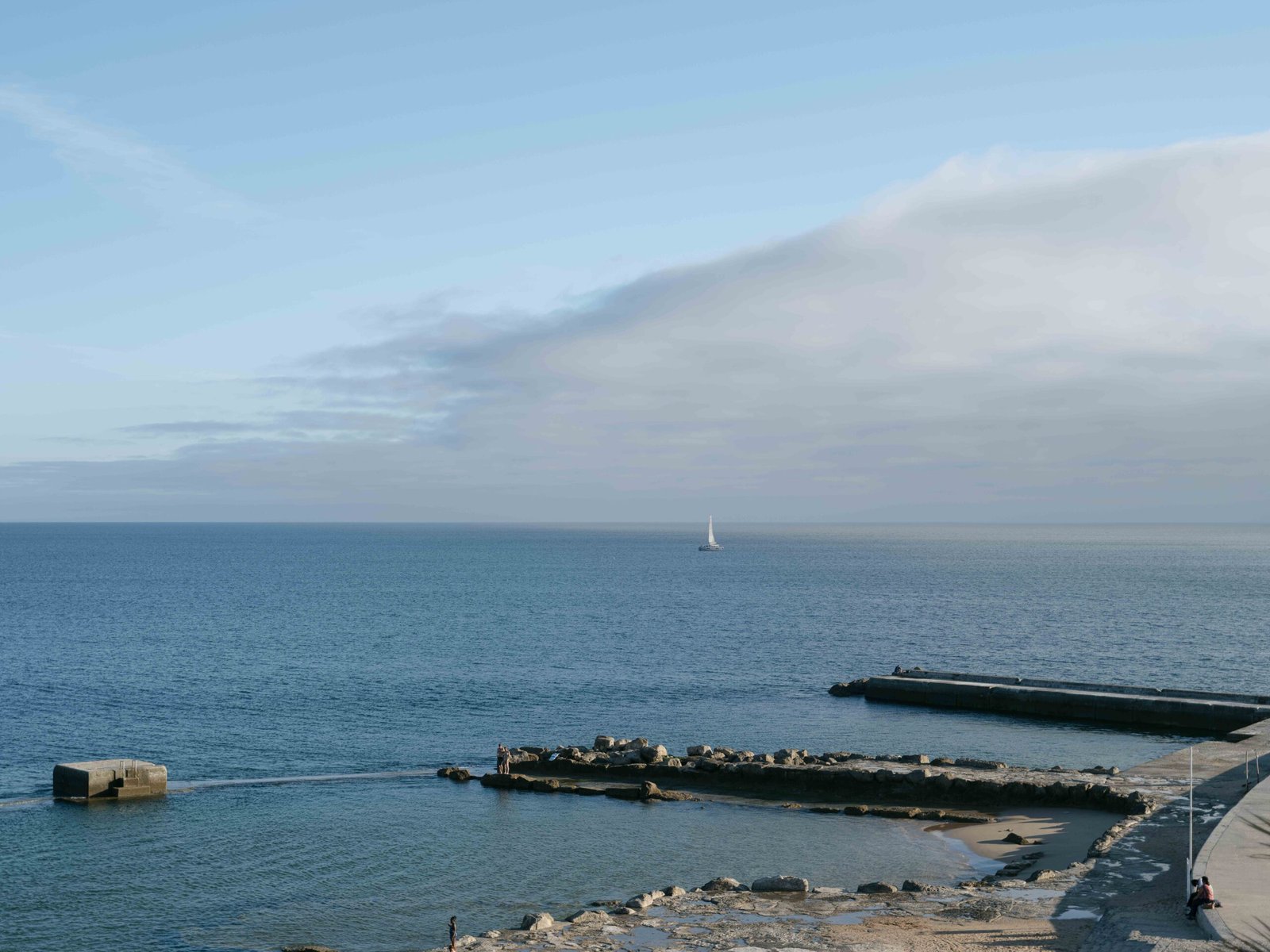 Aerial view of the Atlantic coastline near Lisbon with a stone breakwater in soft evening light