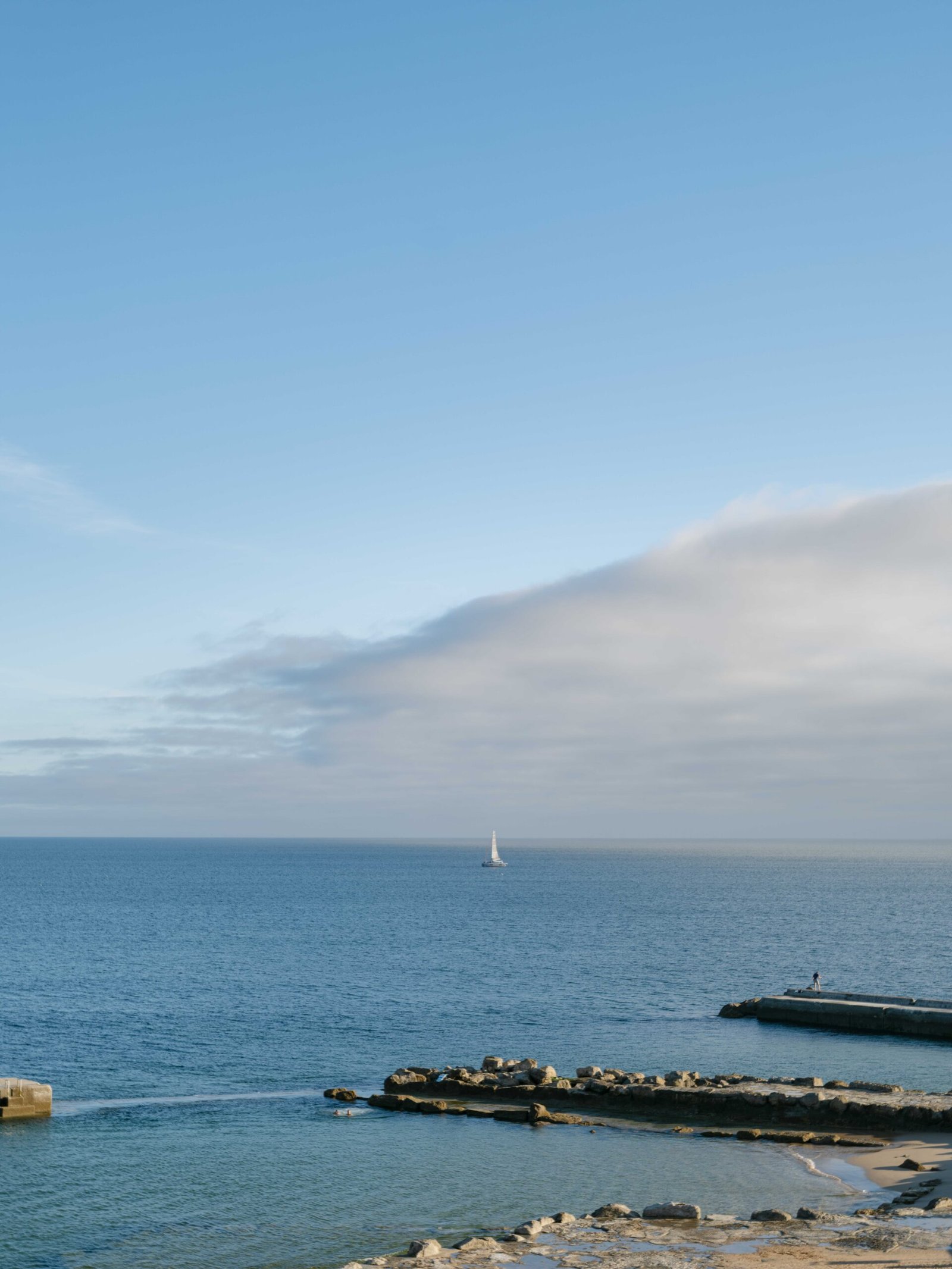 Sailboat passing a stone jetty on the Lisbon coast in soft evening light