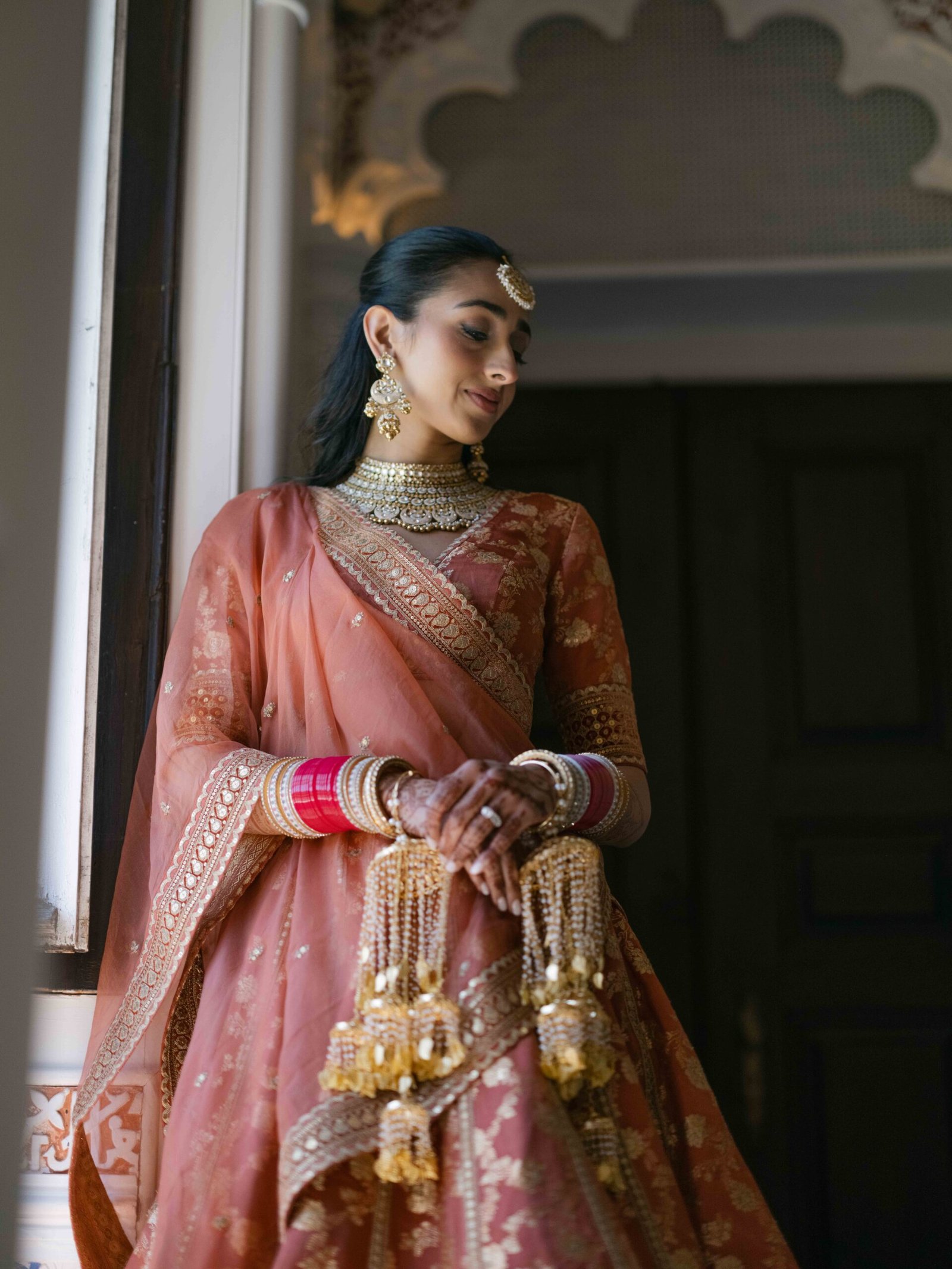 Indian bride in a pink lehenga with kaleere standing in an arched doorway in Lisbon