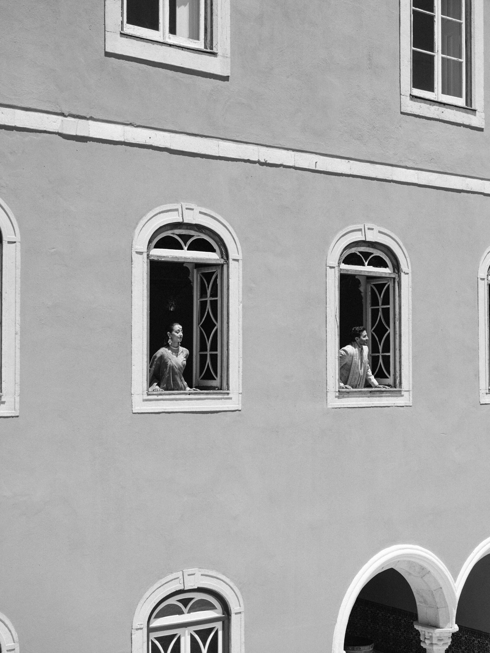 Wedding guests getting ready by arched windows on a pastel façade in Lisbon