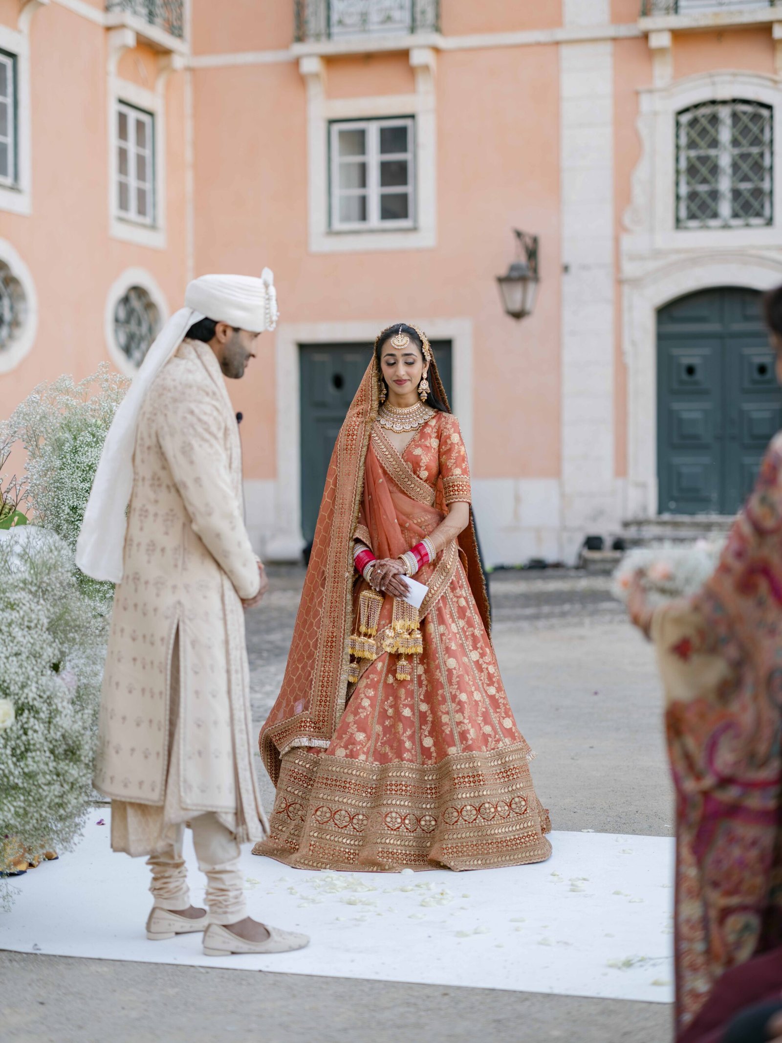 Indian bride in a coral lehenga with the groom in a palace courtyard in Lisbon, soft evening light