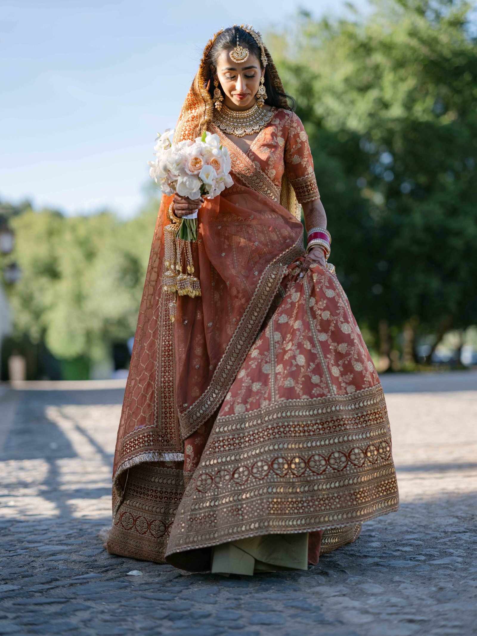 Indian bride in a lehenga walking a cobblestone path in Lisbon at golden hour
