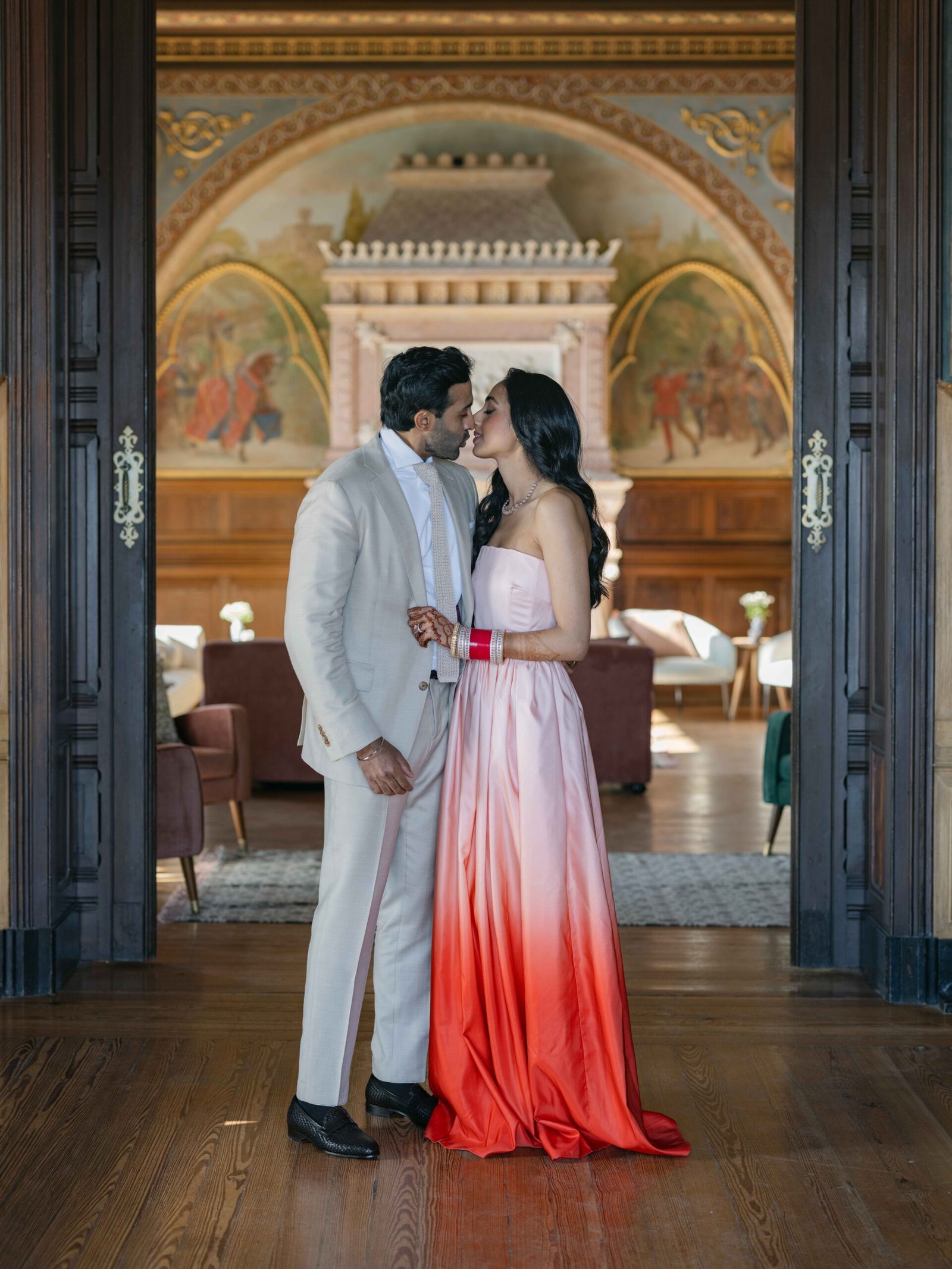 Bride in an ombré gown kissing the groom in a frescoed hallway in Lisbon