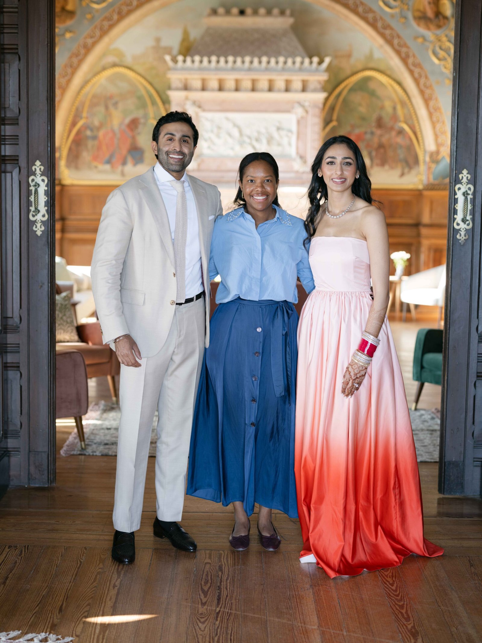 Bride in an ombré gown with the groom and a guest in a frescoed hall in Lisbon, warm evening light