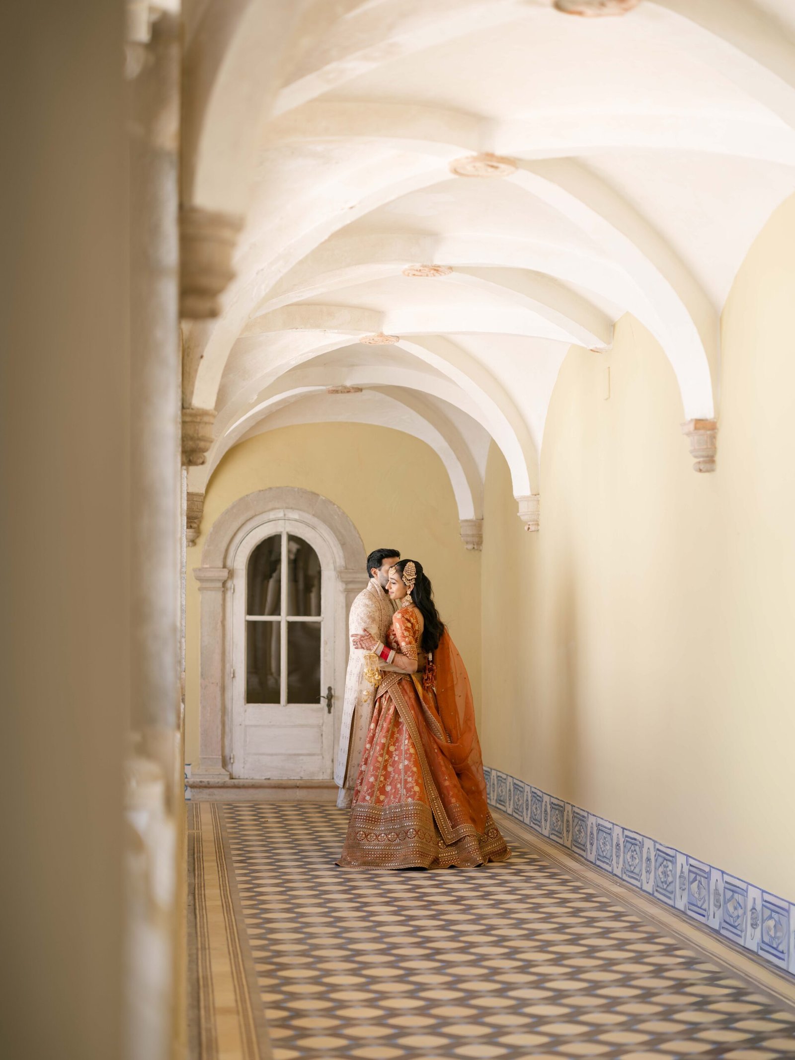Indian couple in wedding attire under a vaulted stone arcade in Lisbon
