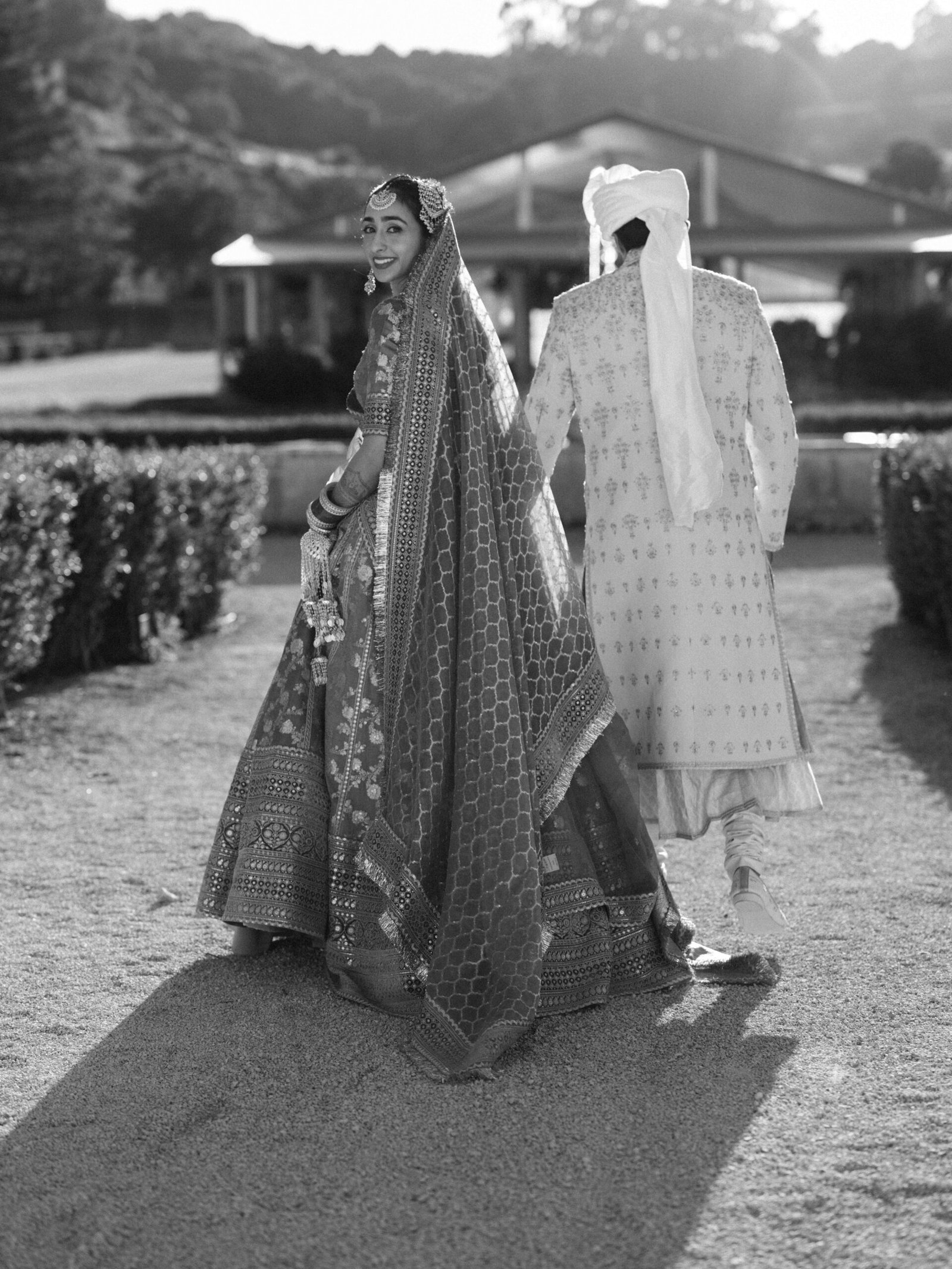 Indian bride in an embroidered lehenga glancing at the groom in a Lisbon garden at golden hour