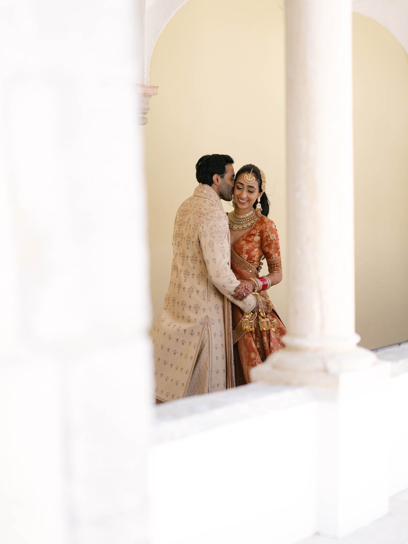 Indian couple in traditional attire embracing under an arched loggia in Lisbon