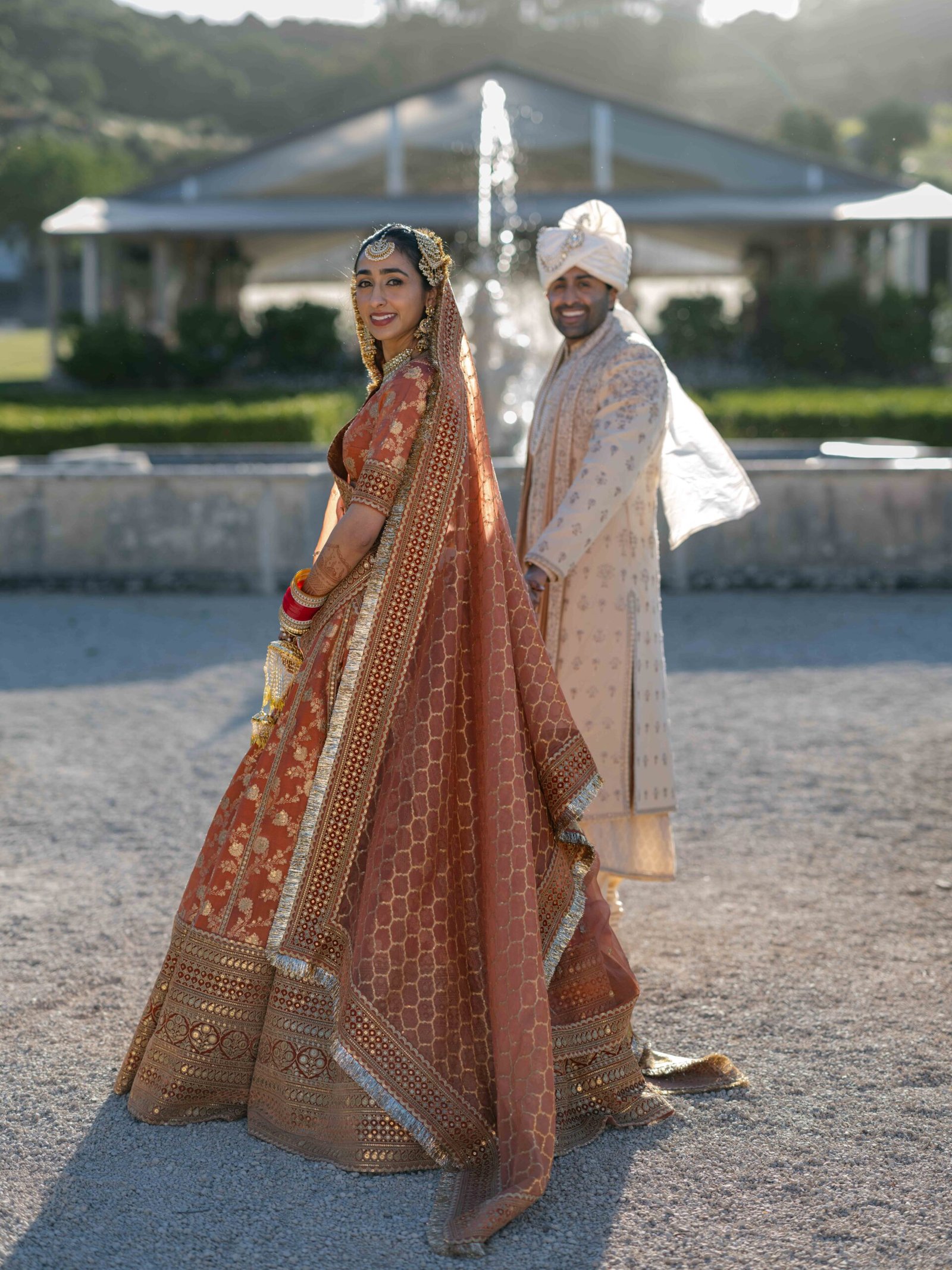 Indian couple by a fountain, the bride in a terracotta lehenga, Lisbon at golden hour