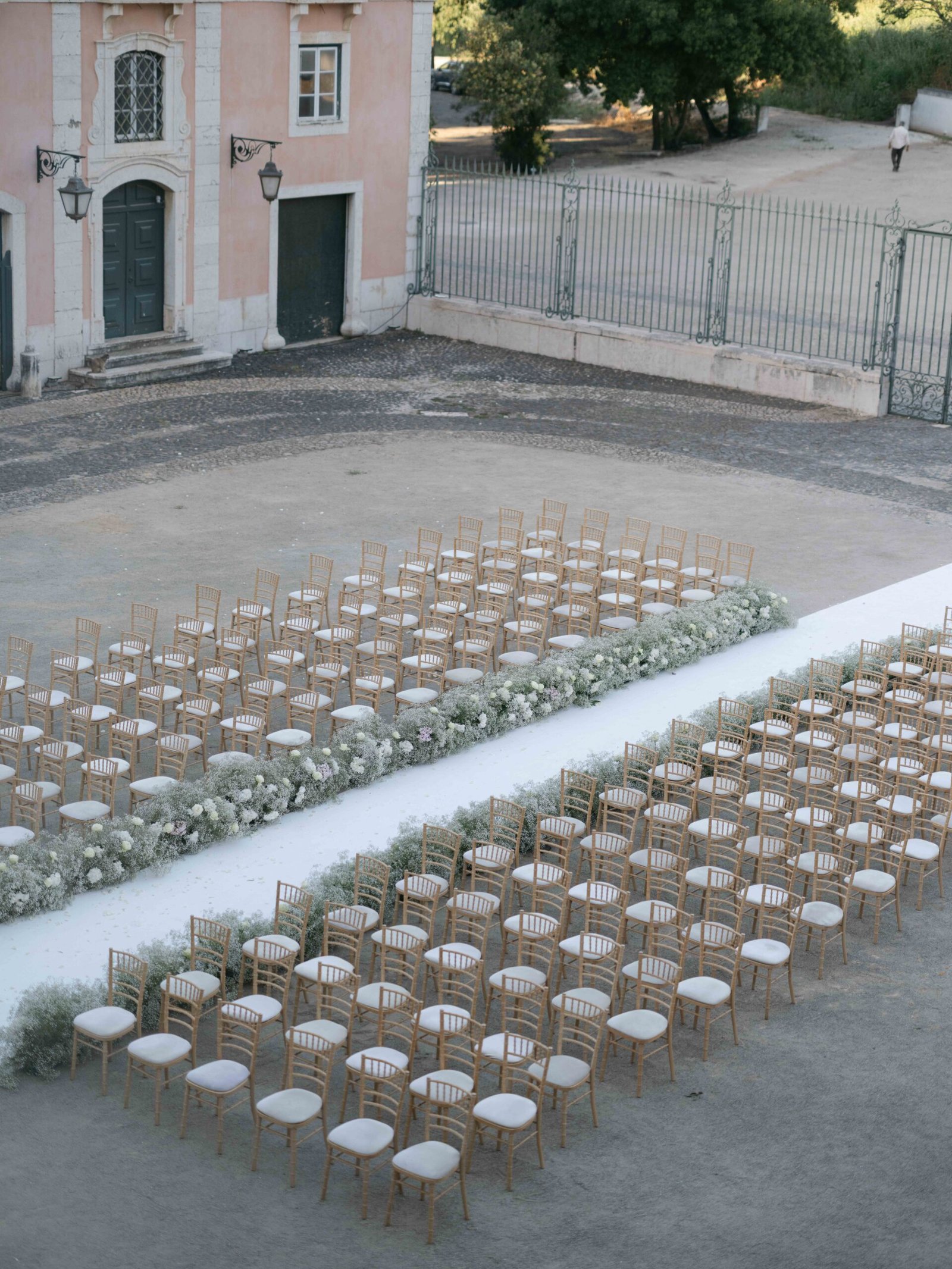 Wedding ceremony aisle with flowers in front of a pink manor house near Lisbon, golden hour