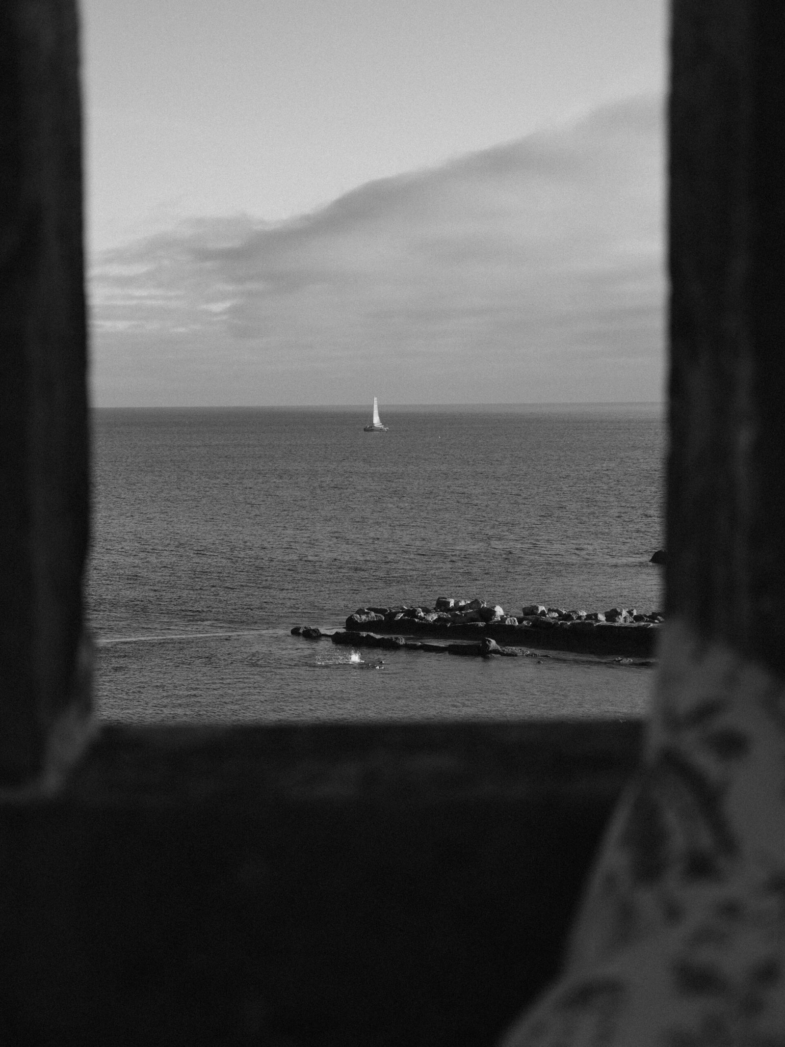 Sailboat on the horizon framed by a window on the Lisbon coast at blue hour