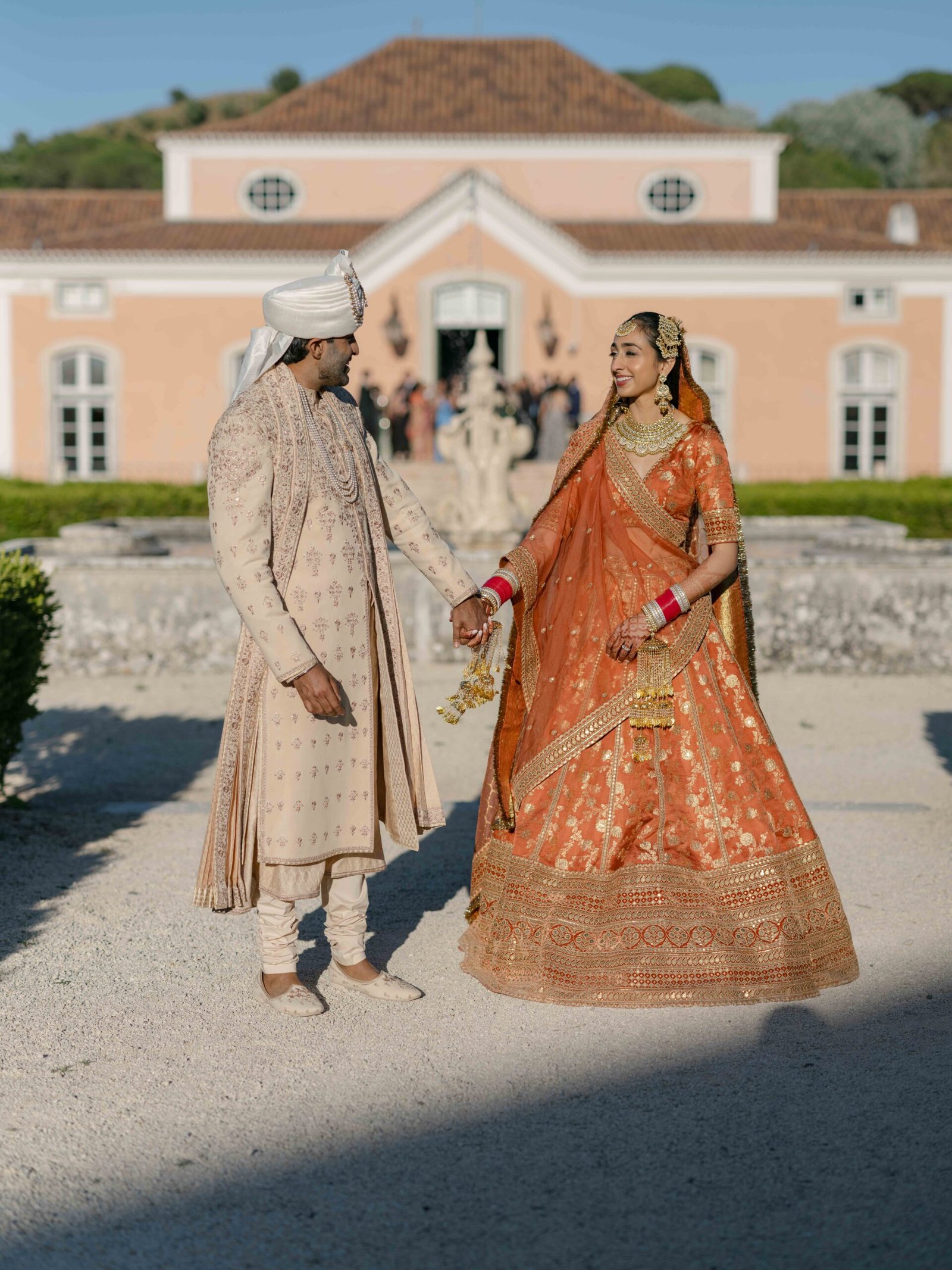 Indian couple in front of a pink manor house, the bride in an orange lehenga, Lisbon