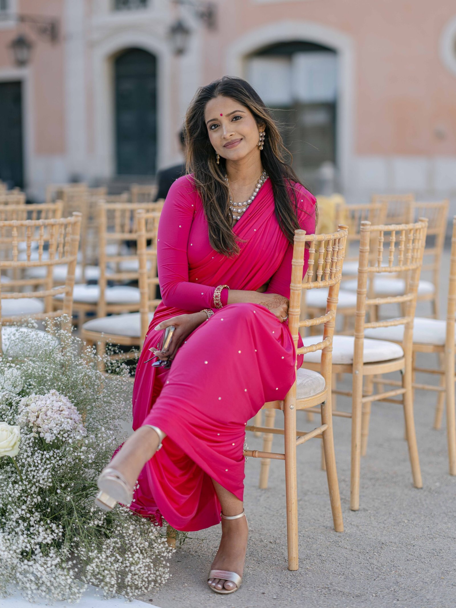 Guest in a pink saree among chiavari chairs at a wedding ceremony in Lisbon, golden hour