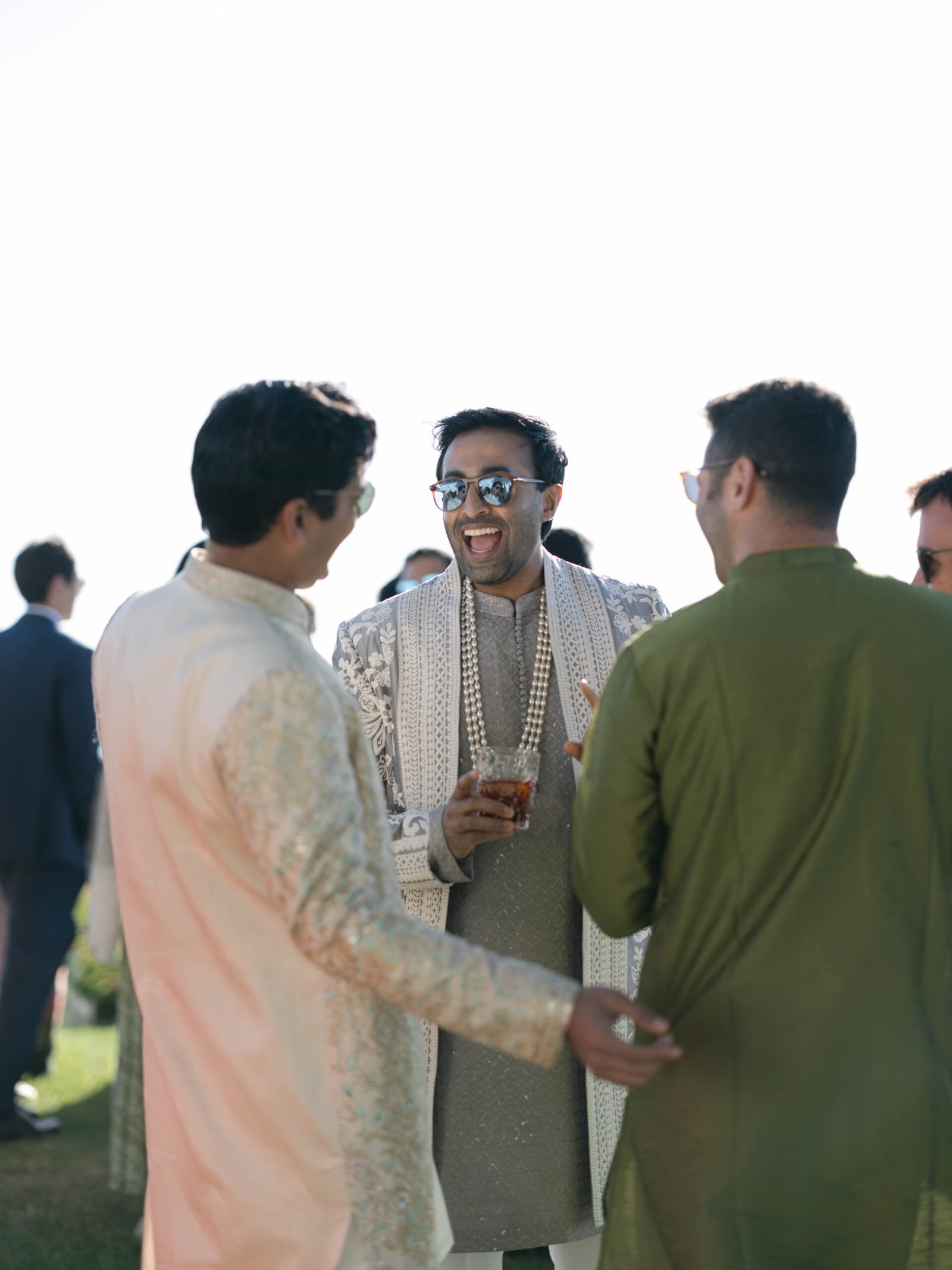 Groom in an embroidered sherwani laughing with guests at the cocktail hour in Lisbon